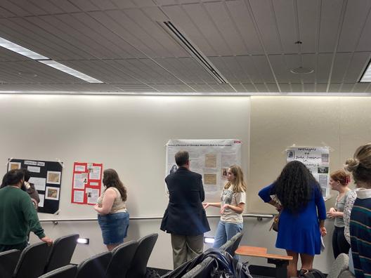 Dr. Ray Irwin looks at a poster while a student describes it and others look on