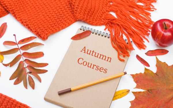 autumn courses written on pad of paper, pencil, leaves, apple and orange knitted scarf