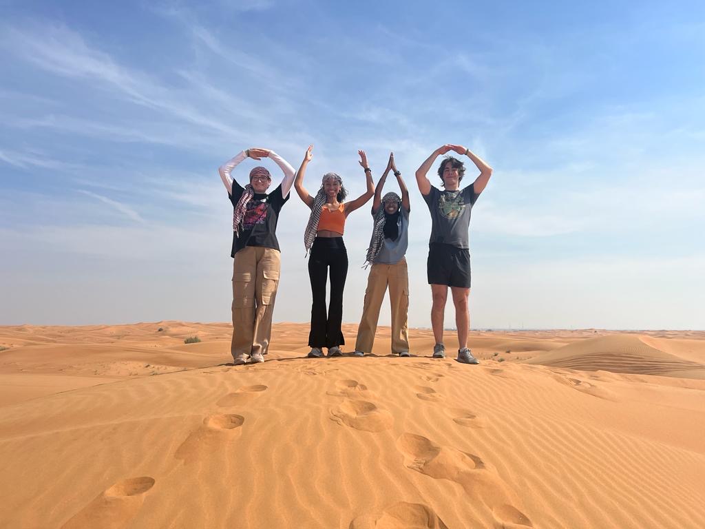 Ohio State Students forming O-H-I-O stance standing on sand in Dubai