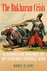 a man in central Asia holding a small canon on a camel that is laying on the ground