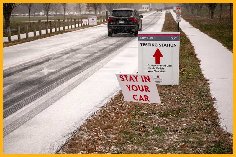 a sign that reads Stay in your car and another sign for a testing station