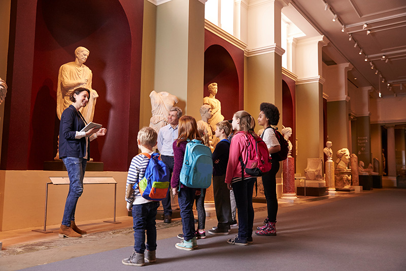 Pupils And Teacher On School Field Trip To Museum With Guide