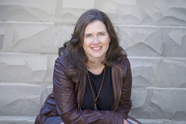 Smiling woman in a leather coat sitting in front of a stone wall