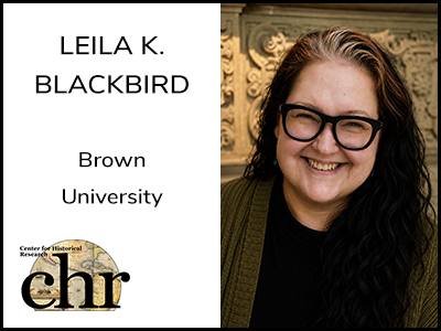 Leila K. Blackbird smiling in front of a carved stone wall