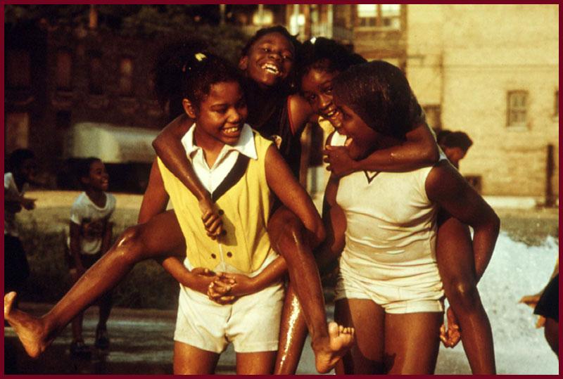 African-American children cool off with water as they play and piggy back ride each other at Woodlawn Community, Chicago, Iillinois, Illinois, 1973. Image courtesy John White/US National Archives. (Photo via Smith Collection/Gado/Getty Images).