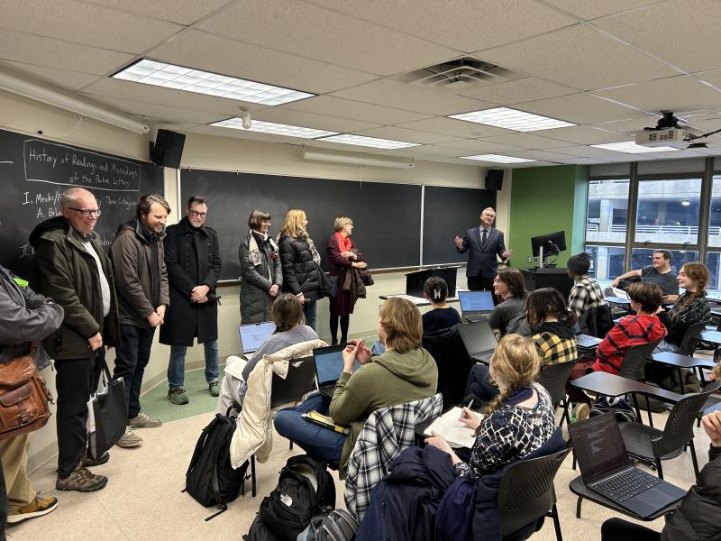 history faculty standing in a classroom while students seated at desks look on
