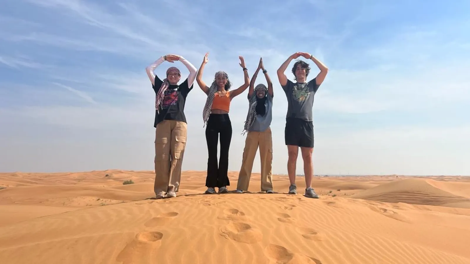 Ohio State Students forming O-H-I-O stance standing on sand in Dubai