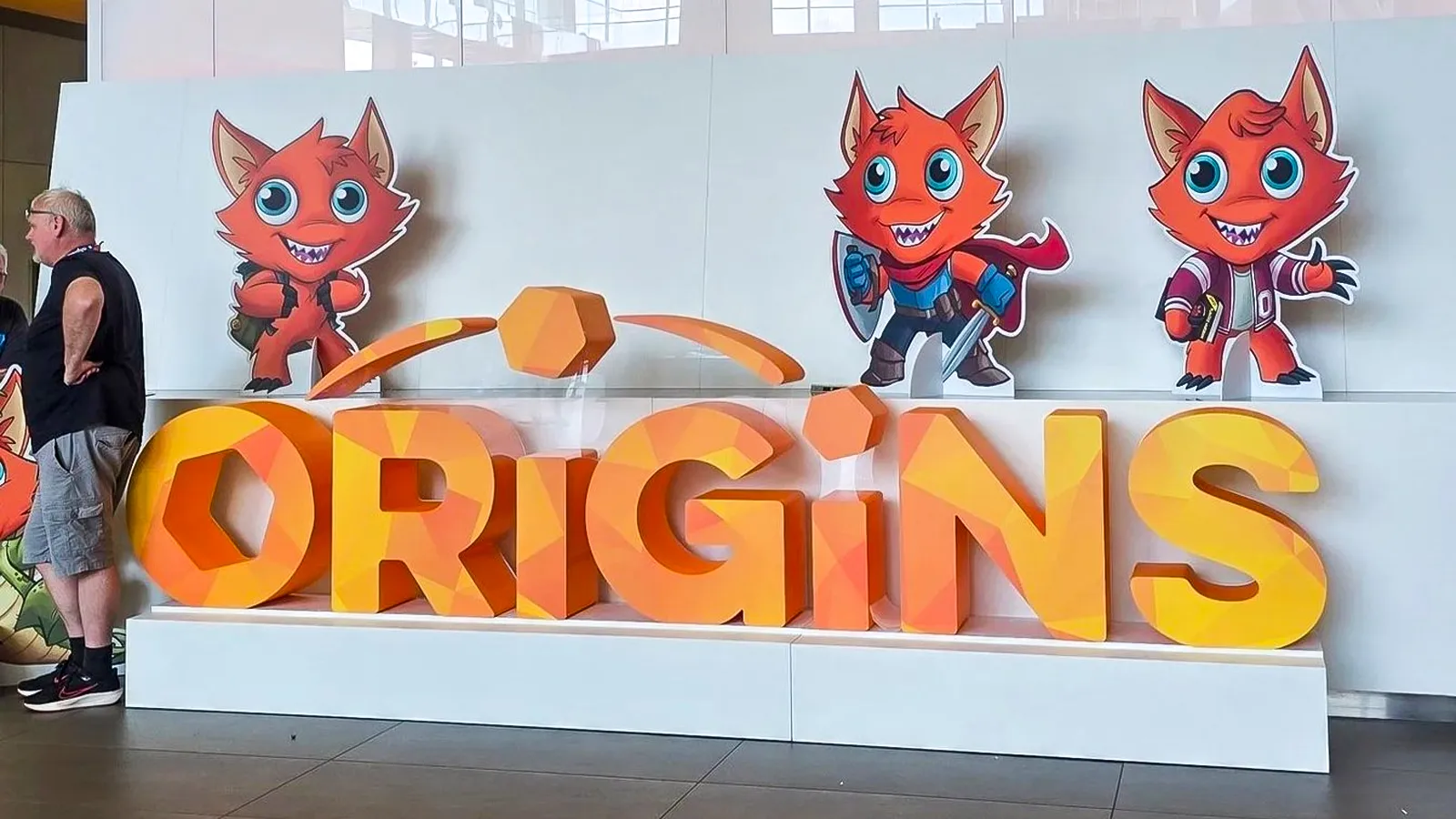 Origins Game Fair sign with attendees standing nearby