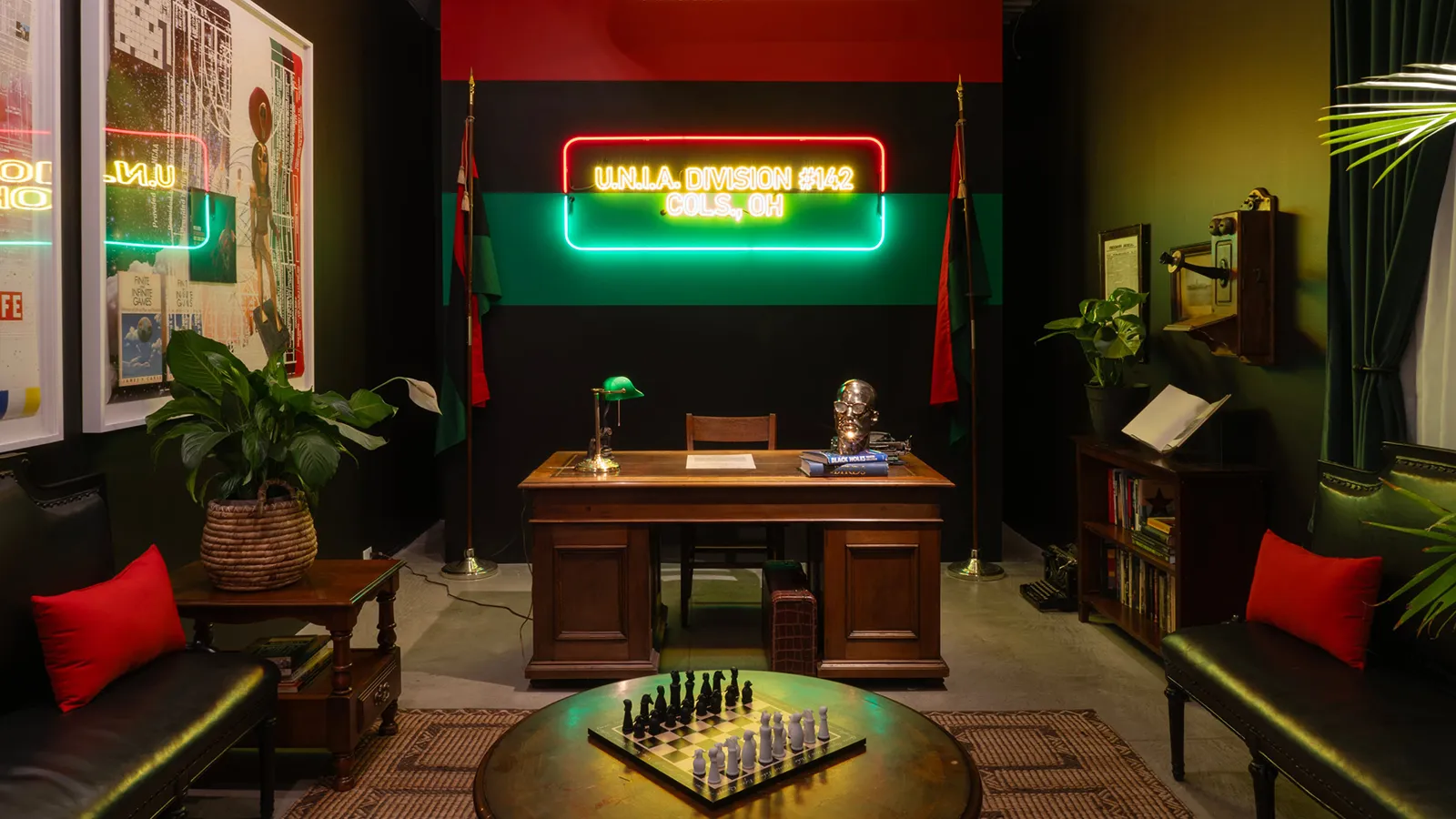 installation view of Tavares Strachan’s "U.N.I.A. Tea Room" depicting an office with a prominent desk and a UNIA Division #142 sign in neon