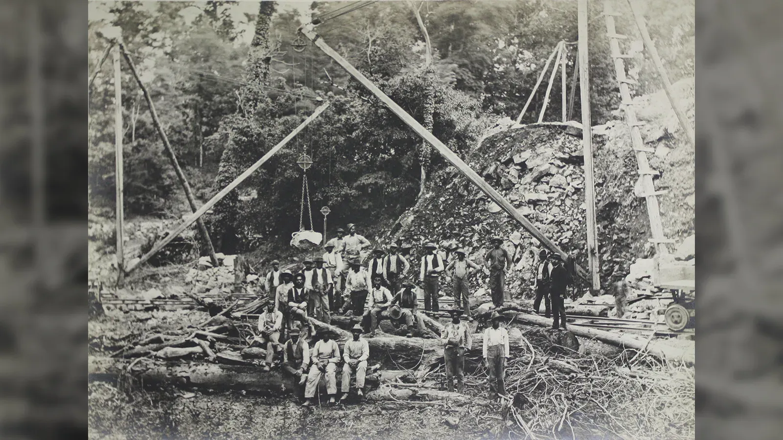 Laborers posing at a heavy construction or quarry site utilizing a large wooden derrick crane system