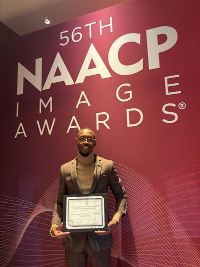 Damarius Johnson holding certificate and standing in front of NAACP Image Awards sign