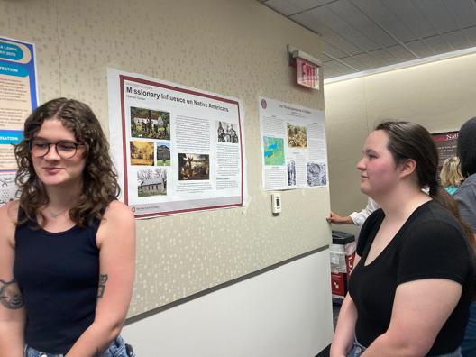 two students standing in front of a poster