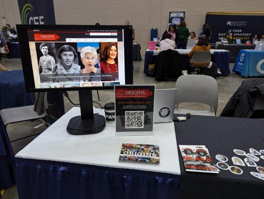 a table with a computer monitor, postcards and signage