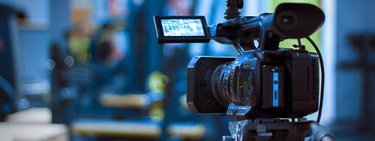 a video camera on a tripod, people sitting in seats in background