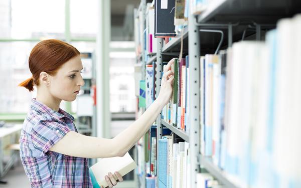woman looking at books in stack at library