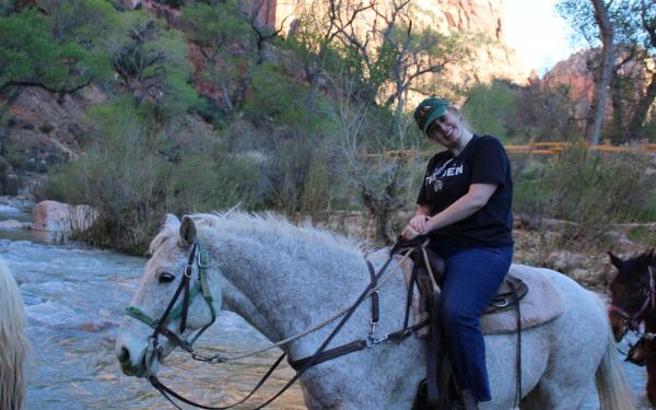 graduate student Tara Godwin on horseback crossing a river in Zion National Park 