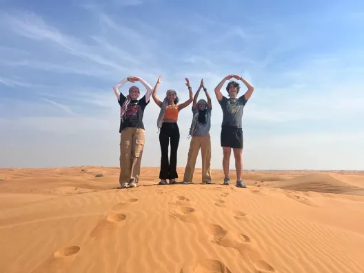 Ohio State Students forming O-H-I-O stance standing on sand in Dubai