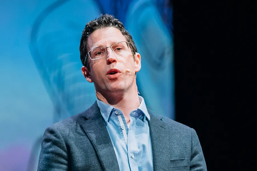 Man with glasses in a suit presenting on stage