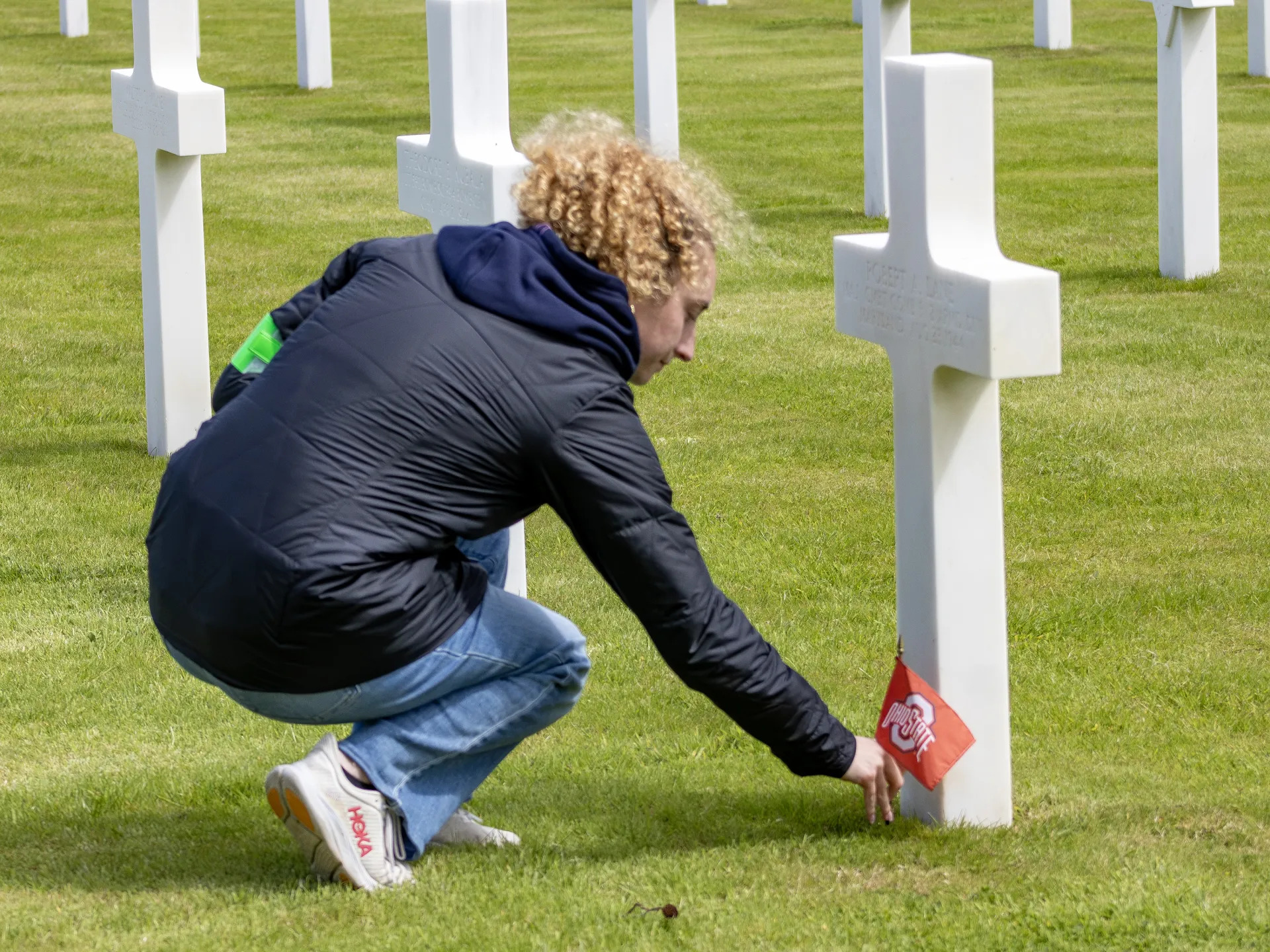 A student placing an Ohio State University flag at the grave of Captain Robert Lane in the Normandy American Cemetery
