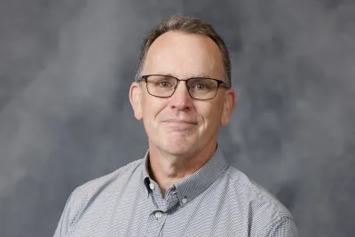 Portrait of Nick Breyfogle, Chair of the Department of History, smiling on a mottled gray background