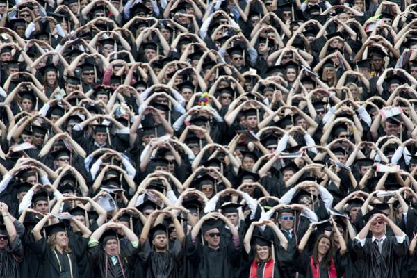 students during commencement with arms raised over heads in O shape