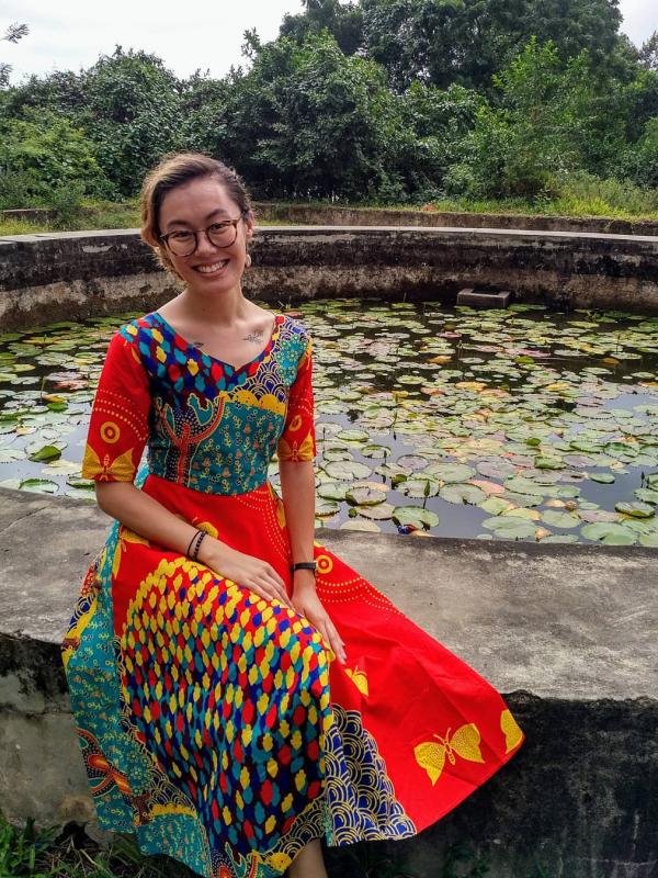 Hyun-Joo sits on a fountain in Zanzibar while wearing a bright Tanzanian dress.