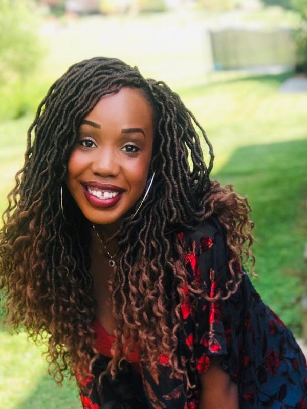 Brown skin, smiling face with dark brown eyes, curly hair locs, wearing a red shirt with roses