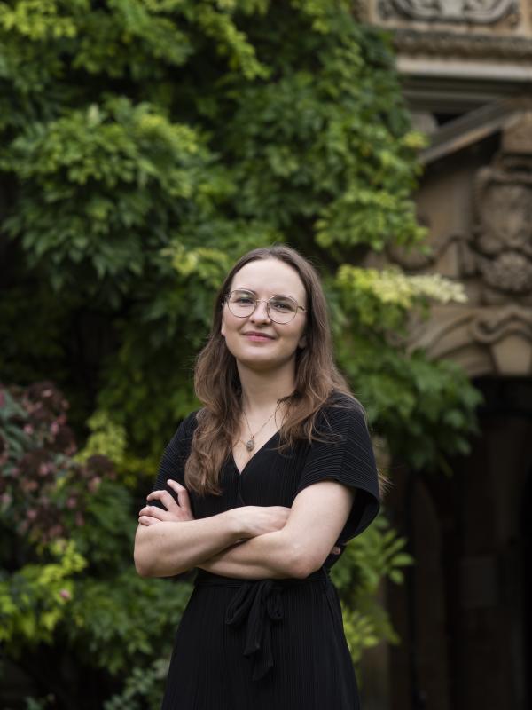Woman with long brown hair standing in front of a leafy background