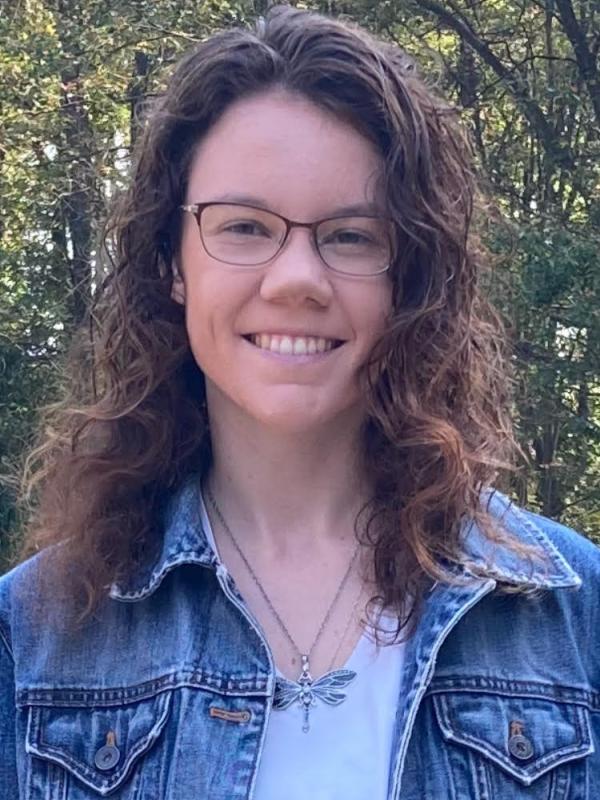 A photo of Emily wearing a blue jacket with trees in the background.