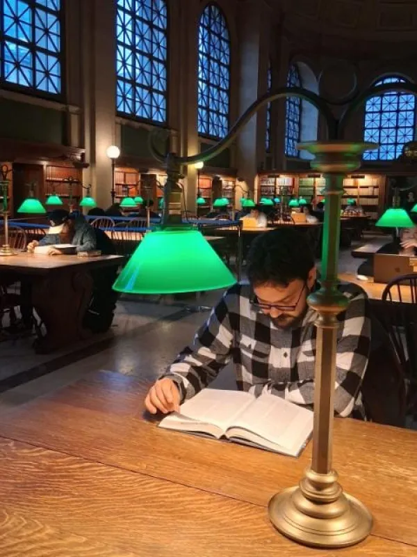 David Longo sitting at a desk reading a book in a darkened library