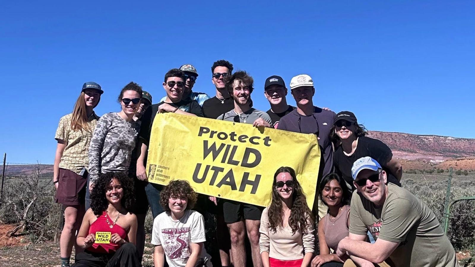 Students and professors holding up a Protect Wild Utah sign in a field in Utah