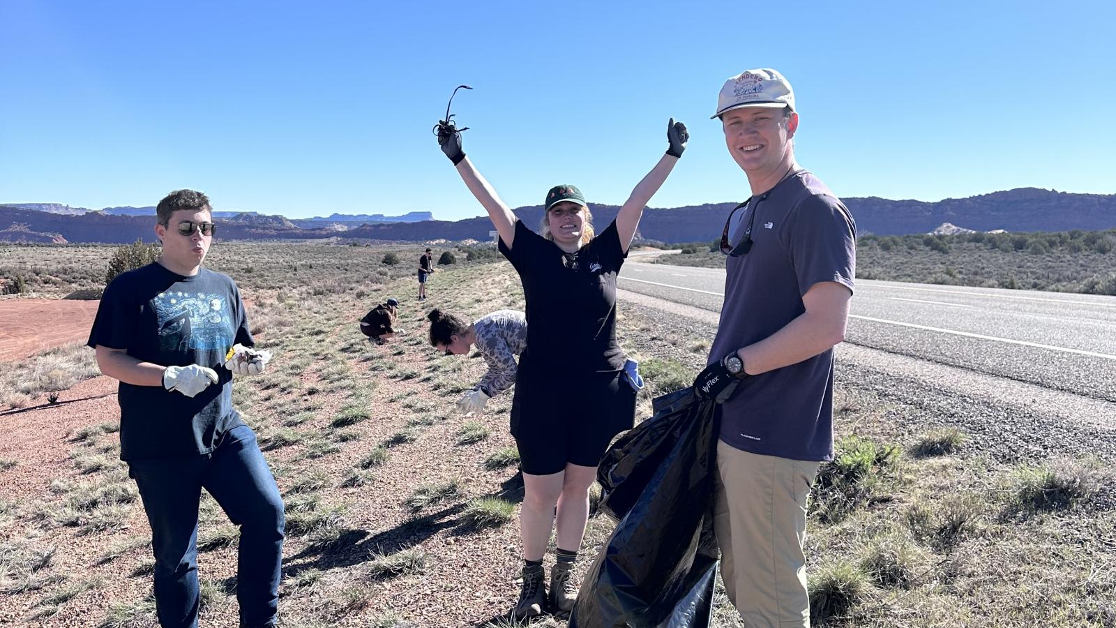 three students picking up trash on the side of a highway in Utah